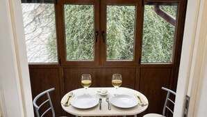 A dining area with a table set for two, a ceiling fan, and a view of trees through the windows. - LightHouse Apartment | 2 BedRoom Apartment (Bucharest)
