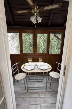 Ein Essbereich mit einem Tisch für zwei Personen, einem Deckenventilator und Blick auf Bäume durch die Fenster.