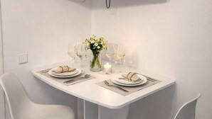 Un comedor con una mesa blanca, dos sillas blancas, un televisor de pantalla plana en la pared mostrando 'NETFLIX', y un florero con flores sobre la mesa.