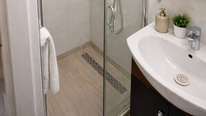 Un baño moderno con ducha envuelta en vidrio, un lavabo blanco y un espejo sobre él.