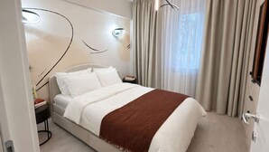 Ein modernes Hotelzimmer mit Bett, Nachttischen, einem Wandbild und einem Fenster mit Vorhängen.