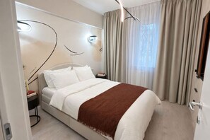Una habitación de hotel moderna con una cama, mesitas de noche, un cuadro en la pared y un ventanal con cortinas.