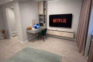 A modern living room with a flat-screen TV mounted on the wall, a desk with a laptop, a green chair, and a small rug on the floor. - The Ascend Luxury Flat | 2 Room Apartment (Bucharest)