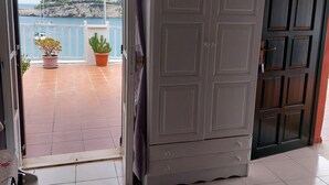 Una puerta abierta que da a un balcón con plantas en macetas y vistas al mar.