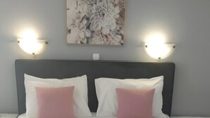 Una cama con disposición de almohadas blancas y rosadas, cabecera gris y una obra de arte floral encima.