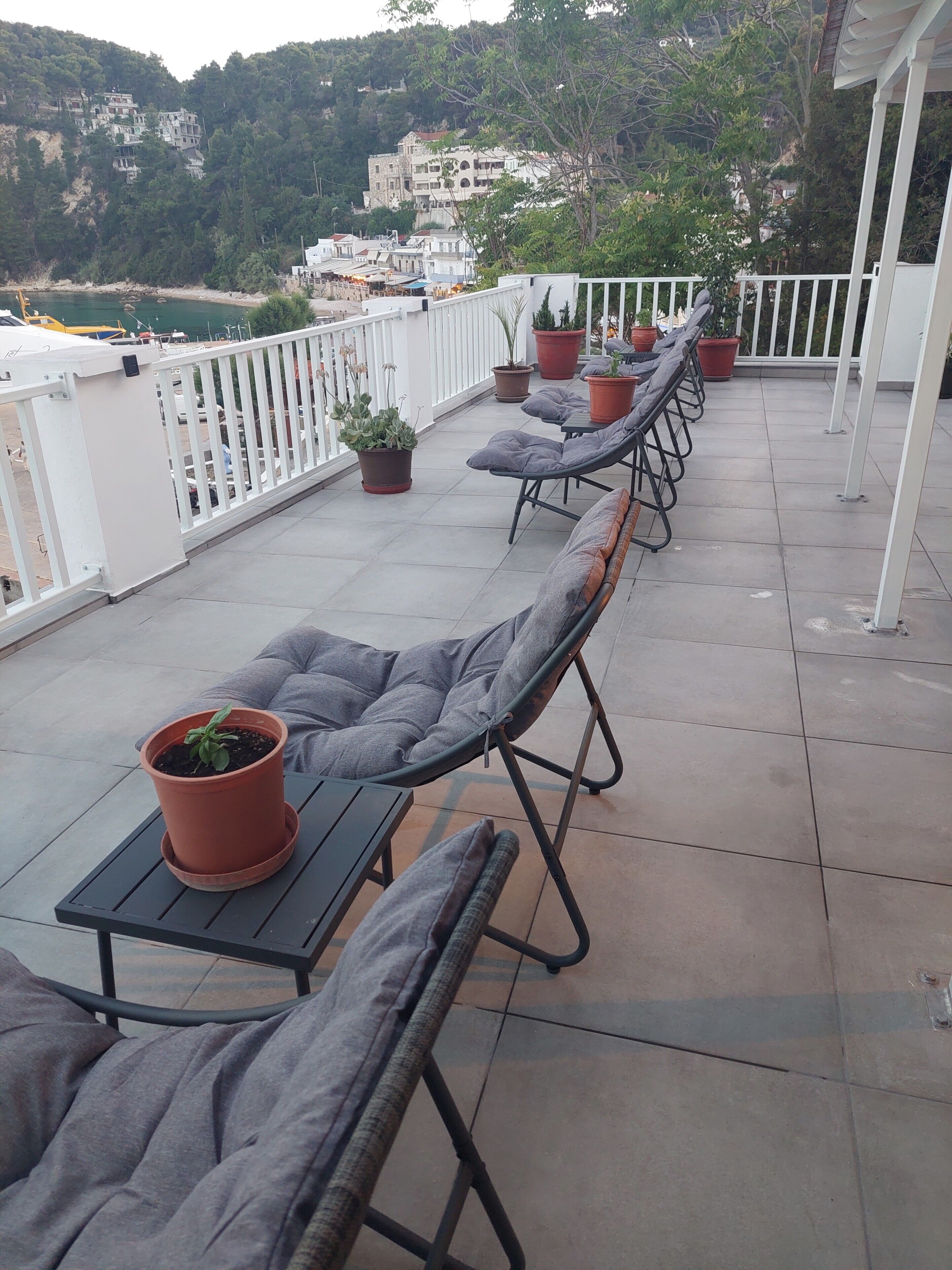 Una terraza con tumbonas, plantas en macetas y vistas a edificios en una colina.