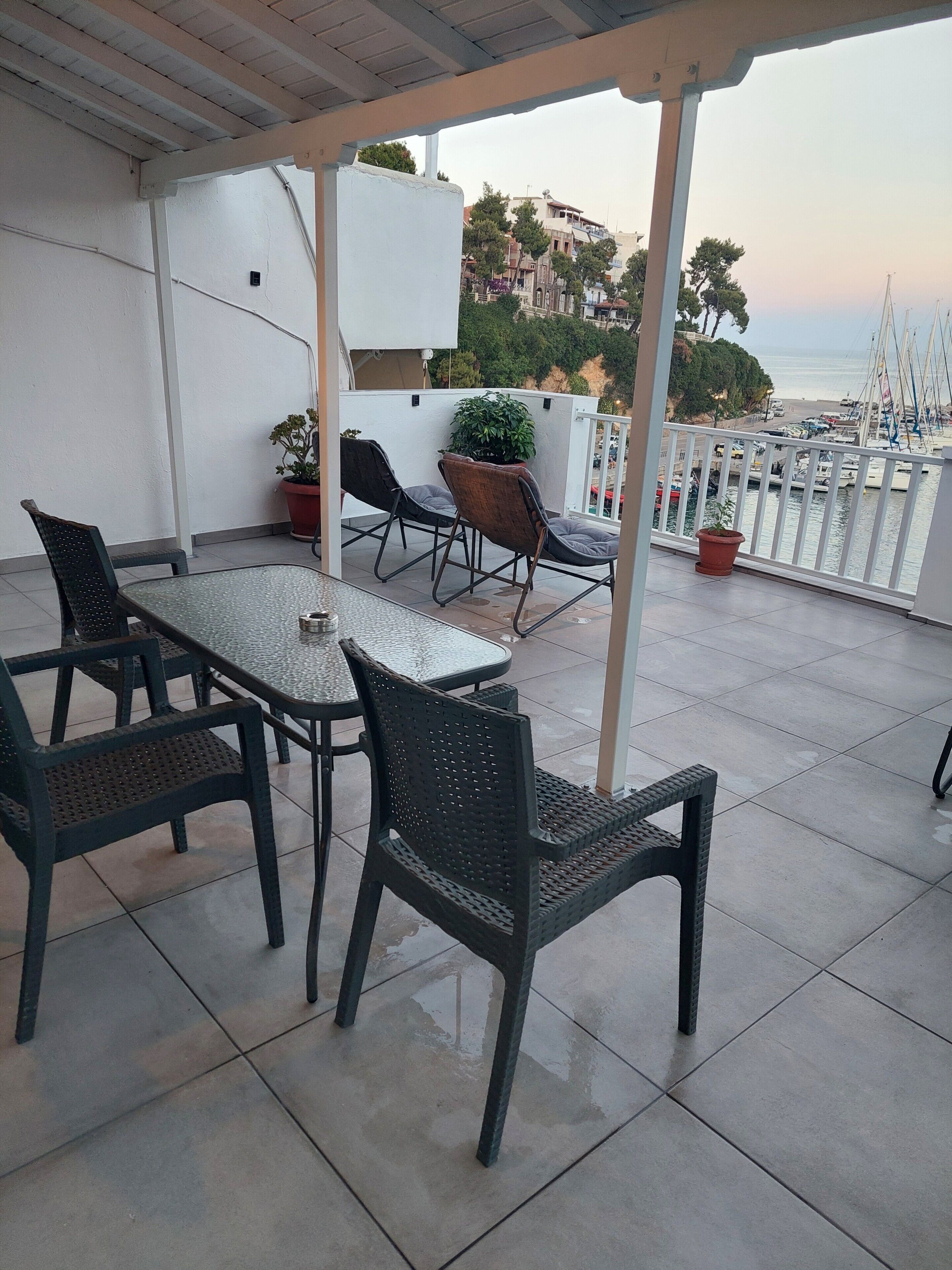 A covered outdoor seating area with a table and chairs, potted plants, and a view of the marina.