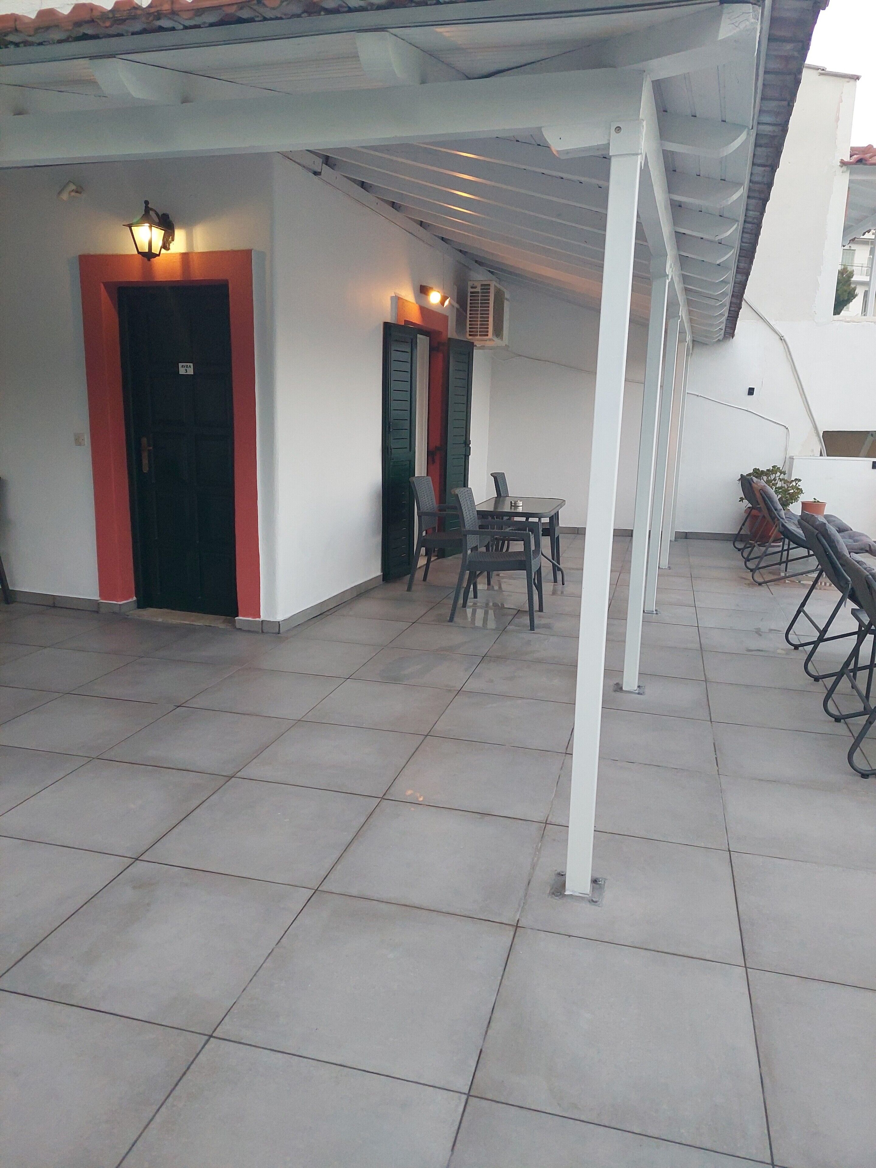 Un patio al aire libre con suelo de baldosas, una mesa con sillas y una zona de estar cubierta con sillones.