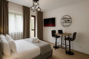 A hotel room with a bed, a TV, a small table with chairs, and a shelf with plants. - The Warmth Loft | Central Apartment (Bucharest)