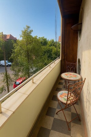 A balcony with a checkered floor, two metal chairs, and a view of a street with cars and trees. - The Warmth Loft | Central Apartment (Bucharest)