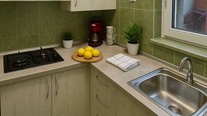 Een keuken met groene tegels, een fornuis, een spoelbak, kastjes, een raam en een koffiezetapparaat.