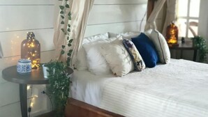 A bed with a canopy, a bedside table with a bottle and a blue and white container, and a plant.