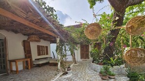 A courtyard with cobblestone flooring, a thatched roof, wicker baskets, and potted plants.