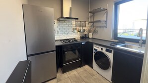 Eine kompakte Küche mit Edelstahl-Kühlschrank, integriertem Backofen, Waschmaschine und einem Fenster für natürliches Licht.