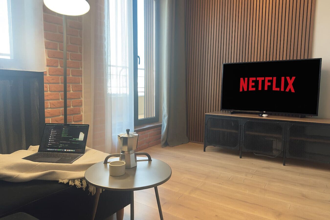 Un salon moderne avec un ordinateur portable posé sur une table, une cafetière et un téléviseur affichant le logo de Netflix.