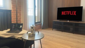 Ein modernes Wohnzimmer mit einem Laptop auf einem Tisch, einer Kaffeemaschine und einem Fernseher, der das Netflix-Logo zeigt.