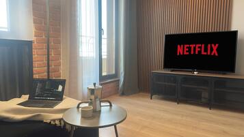 Un salon moderne avec un ordinateur portable posé sur une table, une cafetière et un téléviseur affichant le logo de Netflix.