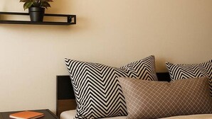 Ein Schlafzimmer mit Bett, Kissen, einem Nachttisch, einem an der Wand befestigten Regal mit Pflanze und einer Korktafel.