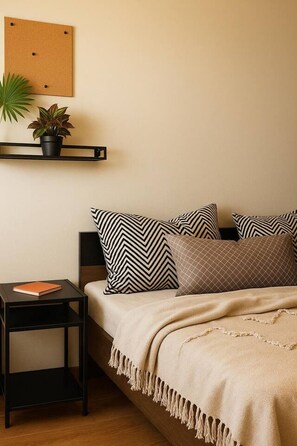 Ein Schlafzimmer mit Bett, Kissen, einem Nachttisch, einem an der Wand befestigten Regal mit Pflanze und einer Korktafel.