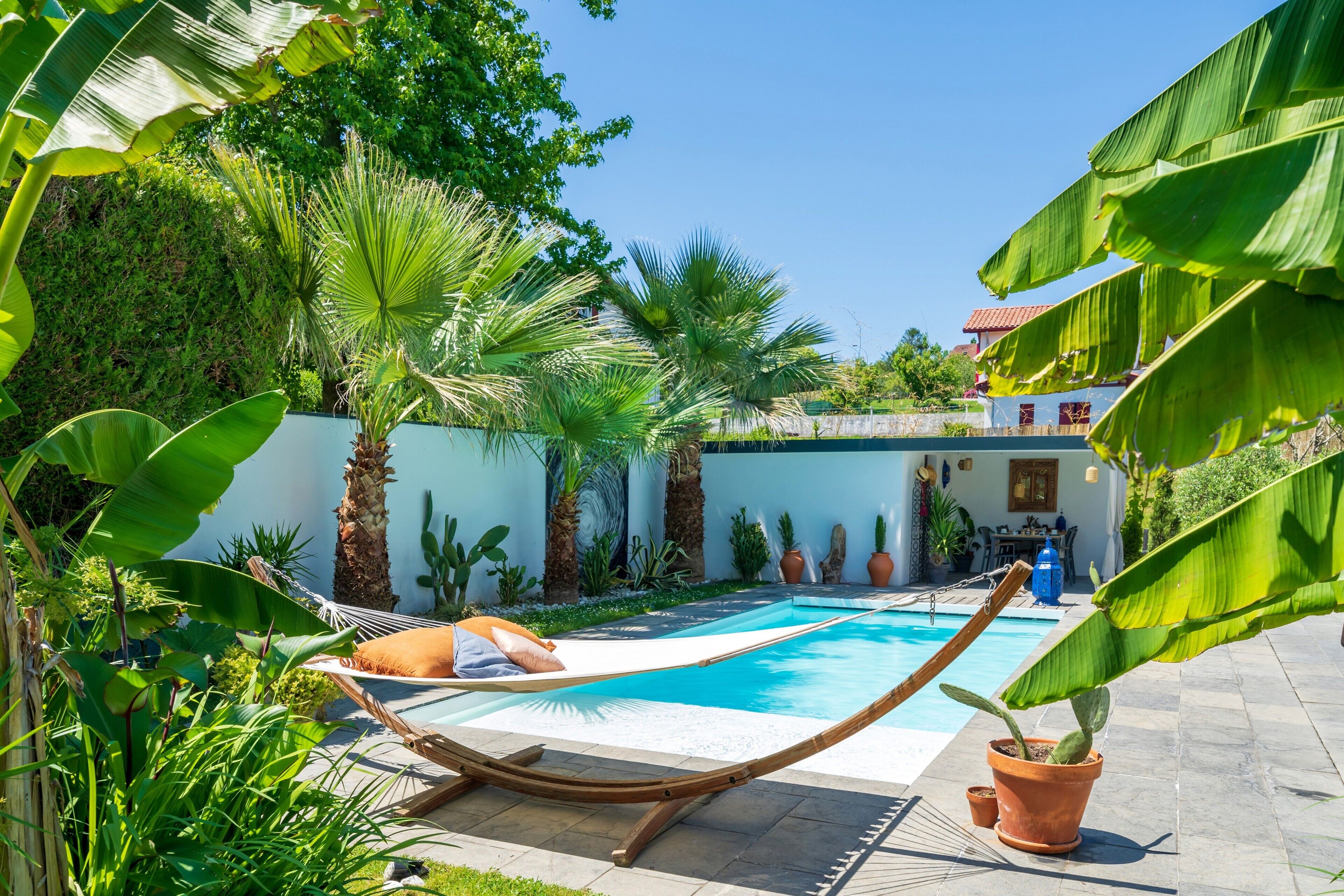 A poolside area with a hammock, potted plants, and a clear blue sky.