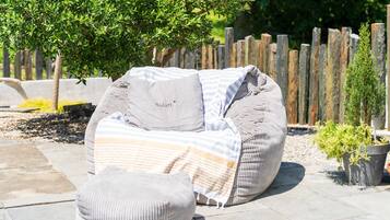 An outdoor seating area with a cushioned bench, a small ottoman, and a potted plant.