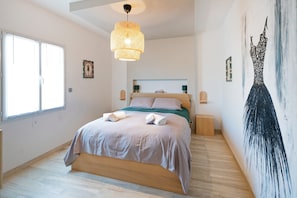 Une chambre à coucher comprenant un lit, des tables de chevet, un luminaire suspendu et un tableau mural.