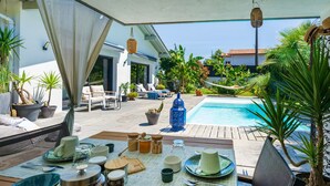 An outdoor dining area with a pool, lounge chairs, and potted plants.