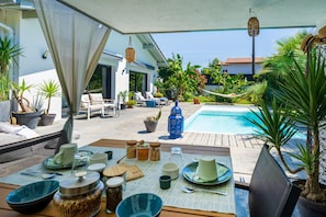 Un espace extérieur aménagé pour les repas, avec une piscine, des chaises et des plantes en pot.