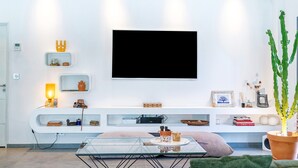 A modern living room with a glass coffee table, green sofa, white entertainment unit, and a large flat-screen TV.