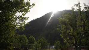 A patio with chairs and a table, surrounded by a fence, overlooking a mountainous landscape. - Applewood Heaven (Bhuntar)