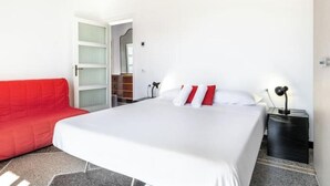 A hotel room with a bed, a red sofa, a nightstand, and a door leading to a bathroom. - Hostdomus - Esther House (Noli)