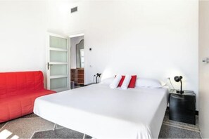 A hotel room with a bed, a red sofa, a nightstand, and a door leading to a bathroom.
