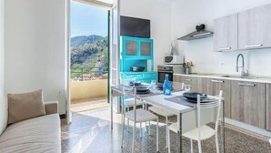 A modern kitchen with a dining area, a view of the outdoors, and a balcony. - Hostdomus - Esther House (Noli)