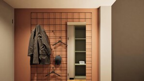 A room with a grid-patterned wall, a coat rack with a jacket, and a shelving unit with folded items. - Essential by Dorint Mannheim Taylor Park (Mannheim)