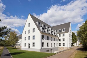 A modern building with multiple windows and a sloped roof, surrounded by a well-maintained lawn and trees. - Essential by Dorint Mannheim Taylor Park (Mannheim)
