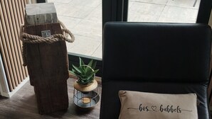A black leather sofa with a cushion that reads 'bos bubbels' and a small wooden stool with a rope.