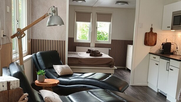 A modern room with a curved sofa, a wooden side table, a lamp, and a view of a kitchen area.