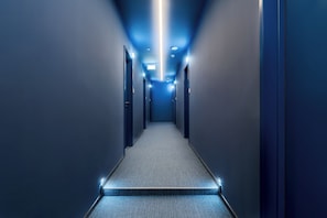 A narrow, well-lit hallway with a carpeted floor and doors on both sides.