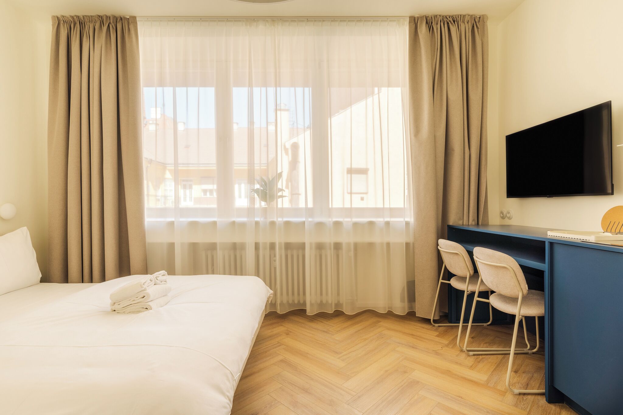 Una habitación de hotel con cama, escritorio y sillas, televisión y ventana con cortinas.