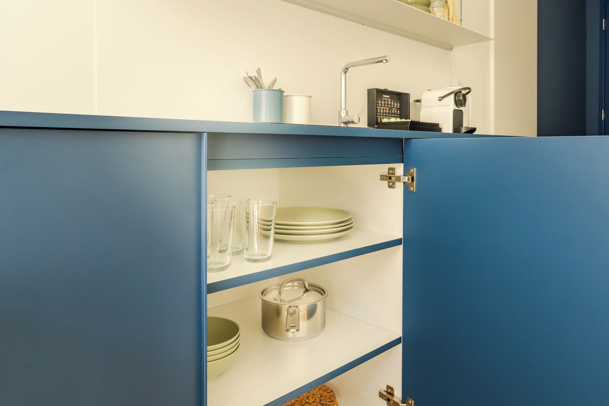 A kitchen with blue cabinets, a coffee maker, and a kettle on the countertop.
