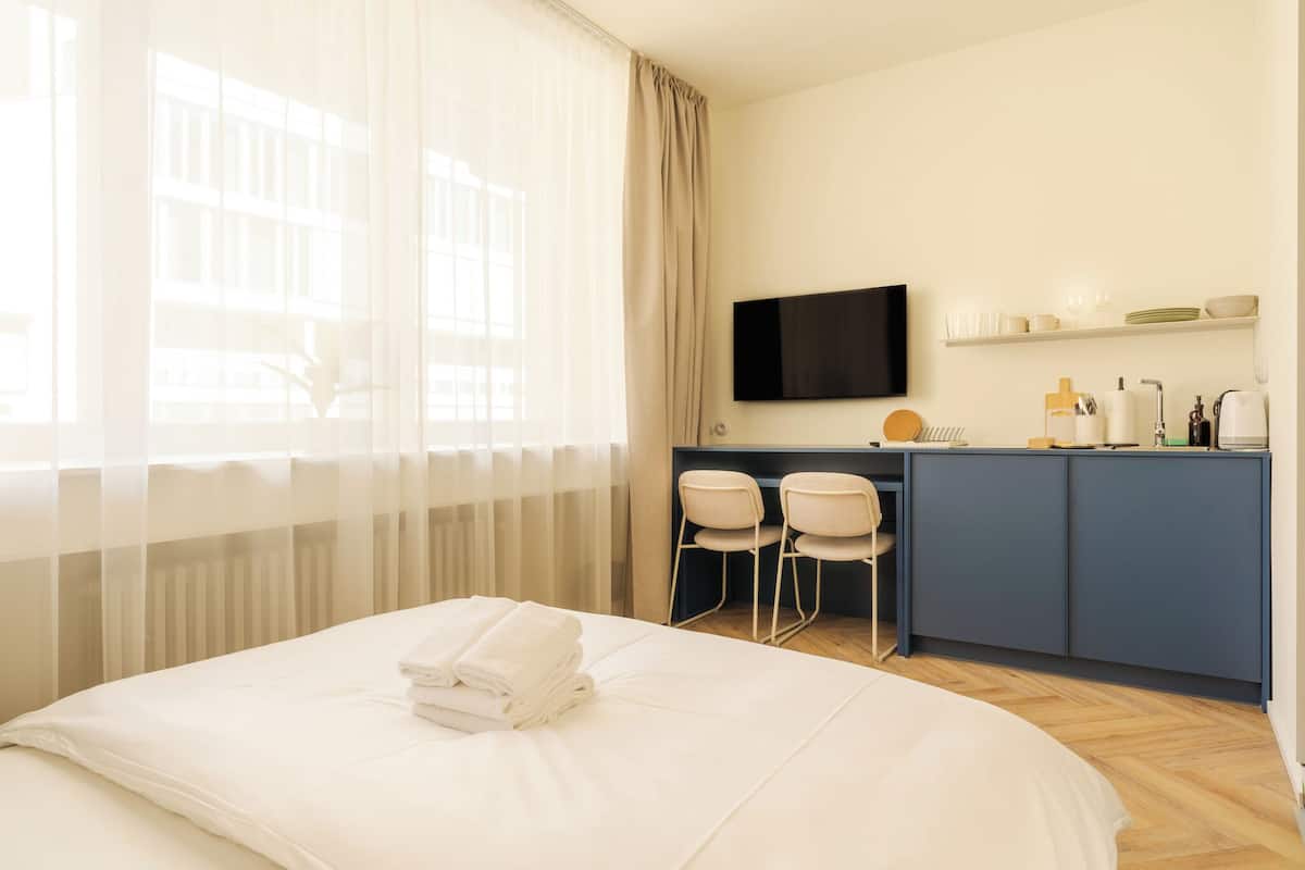 Hotellihuone, jossa on sänky, työpöytä tuoleineen, televisio ja pieni keittiö.