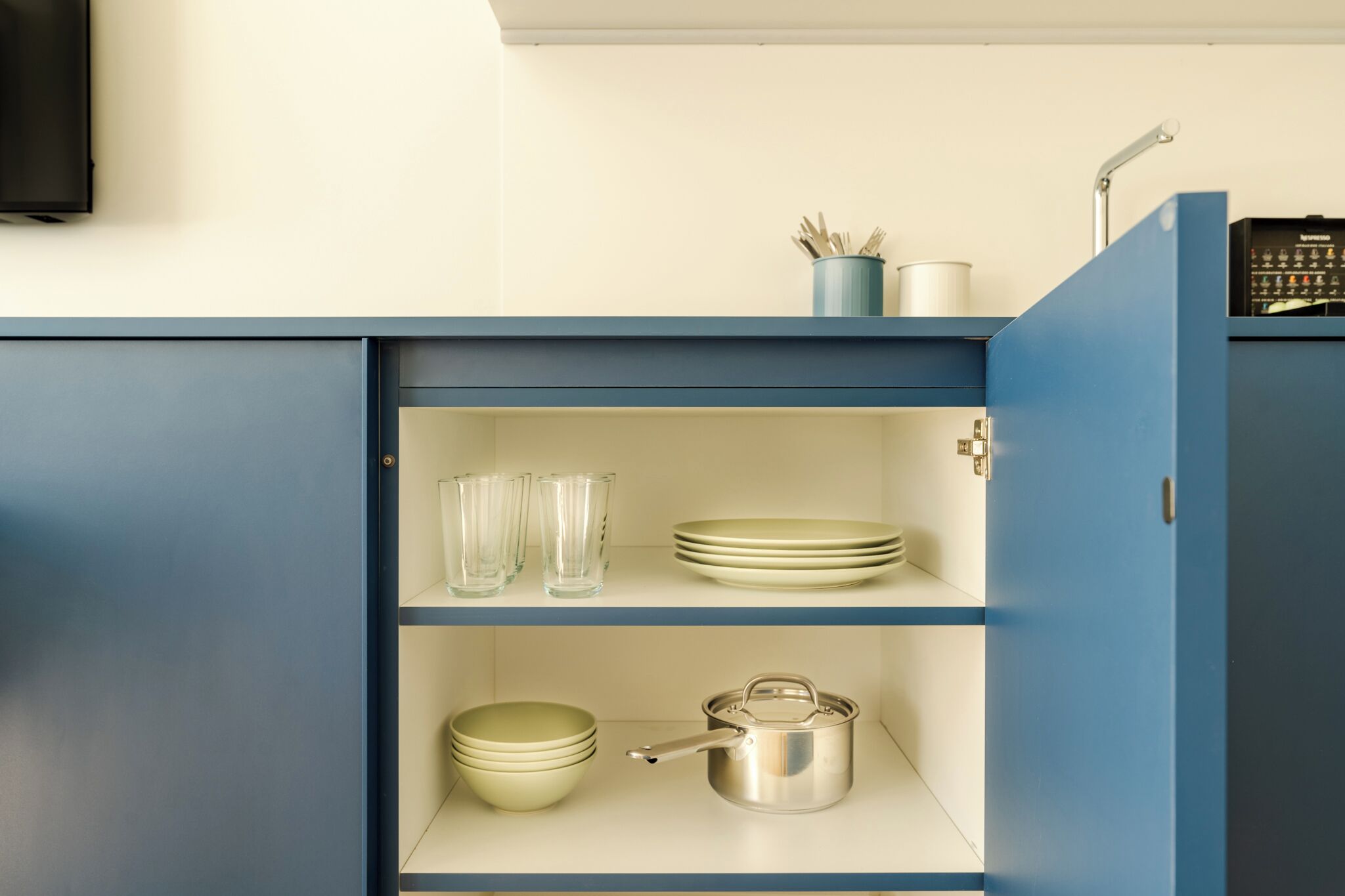 A kitchen with a blue cabinet, clear glass cups, stacked plates, and a stainless steel pot.