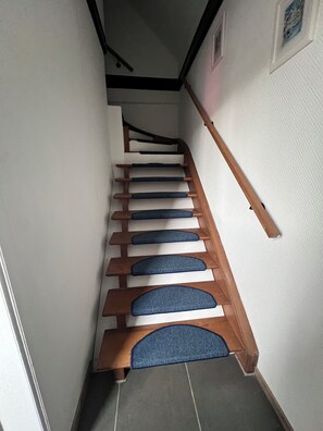 A staircase with wooden steps and blue carpet runners, leading to a landing with a black handrail. - Appartement Cozy et design, position centrale, complètement équipé. (Perwez)
