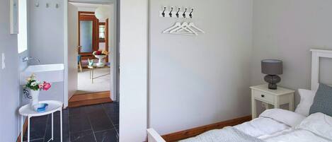 Quarto com cama, mesa de cabeceira, abajur e cabideiro fixado na parede.
