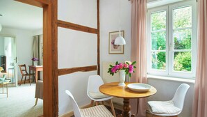 A dining area with a round wooden table, four chairs, a vase with flowers, and a window with curtains. - Artist apartment at Aukrug nature park (Meezen)