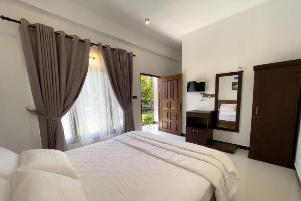 A bedroom with a large bed, curtains, a television, a wardrobe, and a door leading to a balcony.