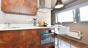A modern kitchen with a central island, stainless steel appliances, and a window providing natural light. - Student Only Marketgait (Dundee)