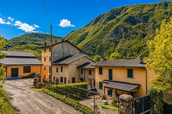A rural village with traditional houses, a dirt road, and lush green hills in the background.