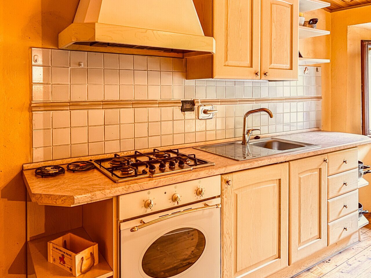 A kitchen with a gas stove, oven, sink, and wooden cabinets.