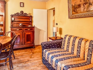 A cozy living room with a wooden dining table, chairs, a sofa, a cabinet, and a painting on the wall.